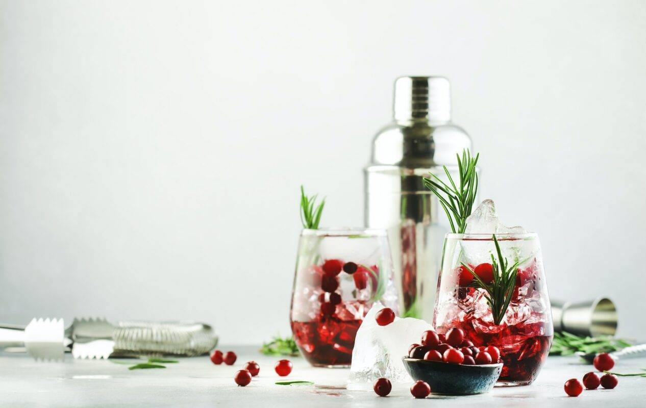 Cranberry cocktail or mocktail with ice, rosemary and red berries in tumbler glass